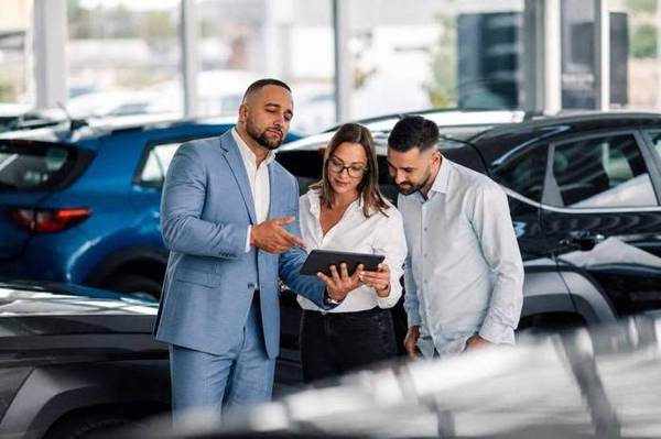 An auto consultant walking a couple through the numbers on a tablet, on a dealership floor